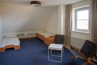Übernachtungszimmer mit Dachschräge, zwei Betten und einer Sitzgruppe